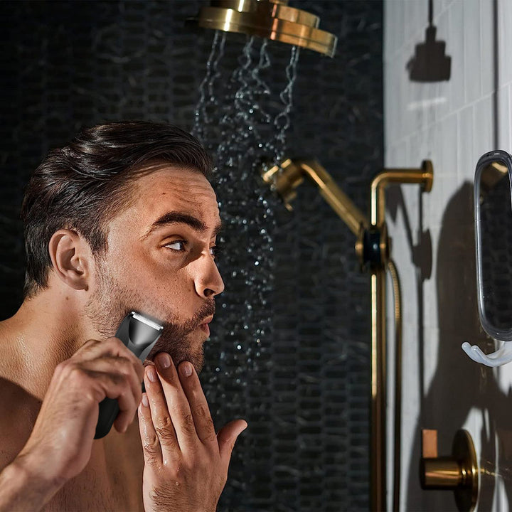 Man grooming his beard with Maxgroom trimmer in steamy shower environment, using mirror